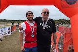 An older man with glasses embraces his son who is in his twenties at the finish line of a race.