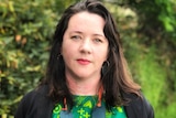 A woman with dark hair wearing a green dress smiles for the camera 