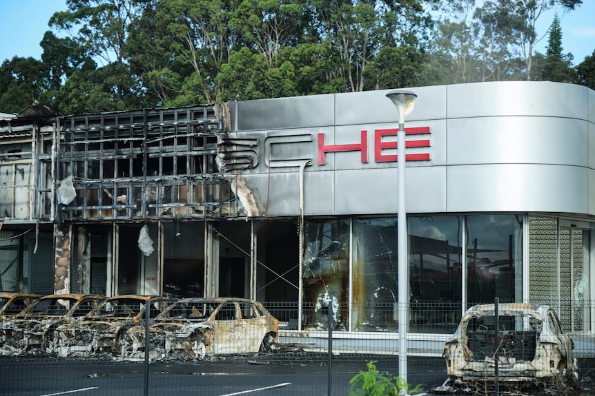 A burnt Porsche car dealership. Its cars and building are badly damaged or destroyed.