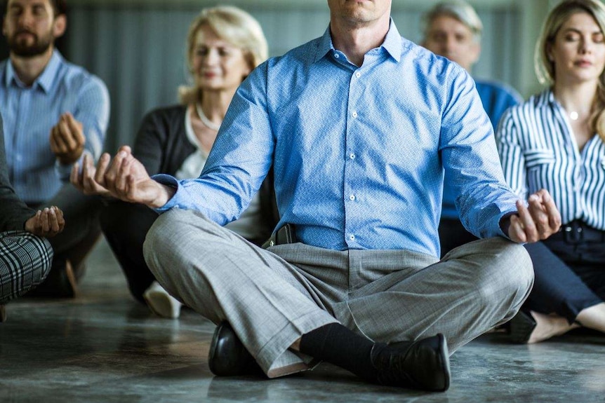 Group of business people sitting with crossed legs holding hands over knees with eyes closed.