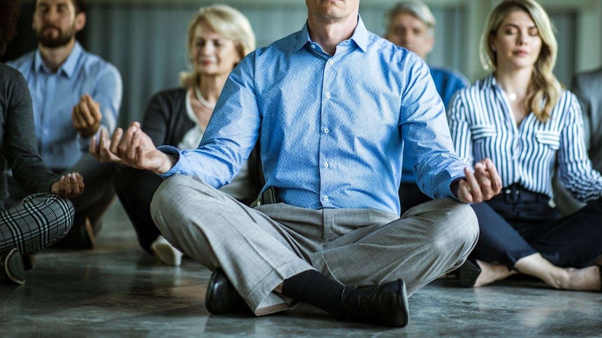 Group of business people sitting with crossed legs holding hands over knees with eyes closed.