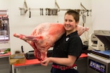 Apprentice butcher Sarah Wadland holding a lamb carcass over her shoulder.