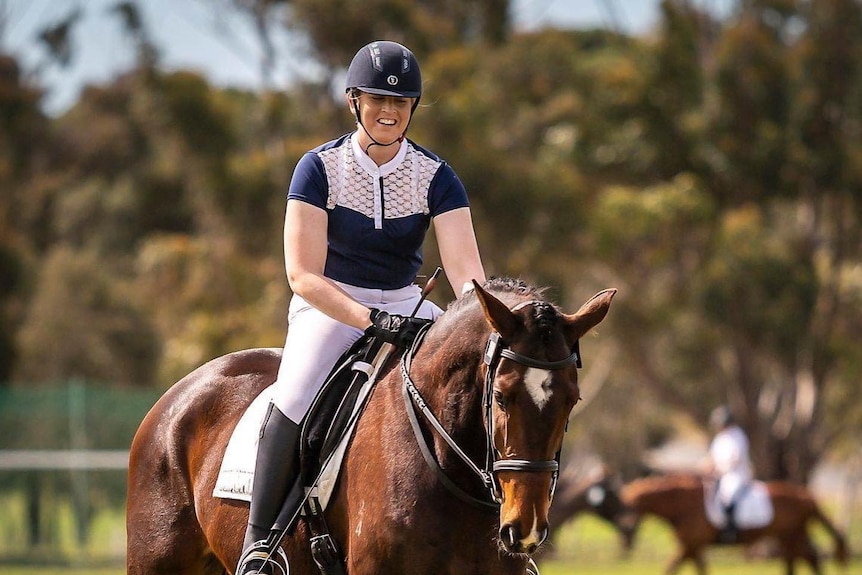 A female para-equestrian rider is on a horse, smiling. 