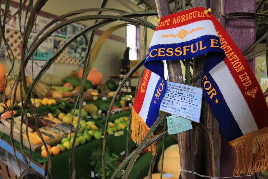 A champion show ribbon pinned to a pole with a fruit and vegetable display in background.
