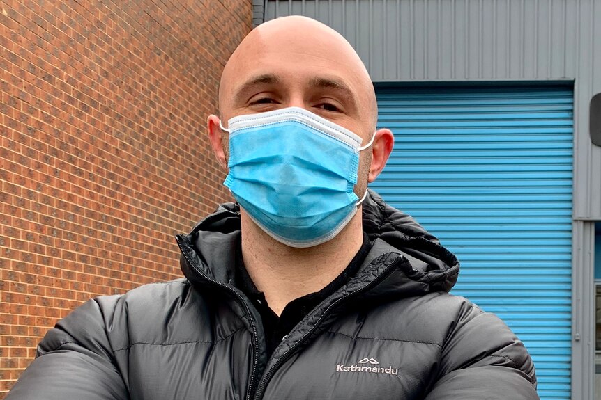 Ben Lustig dressed in a puffer jacket and wearing a mask, stands outside his gym.