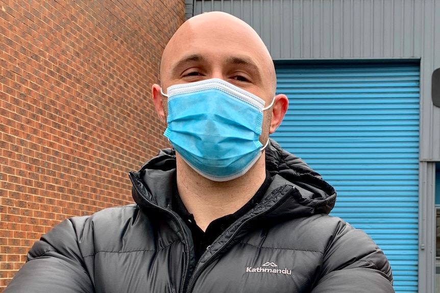 Ben Lustig dressed in a puffer jacket and wearing a mask, stands outside his gym.