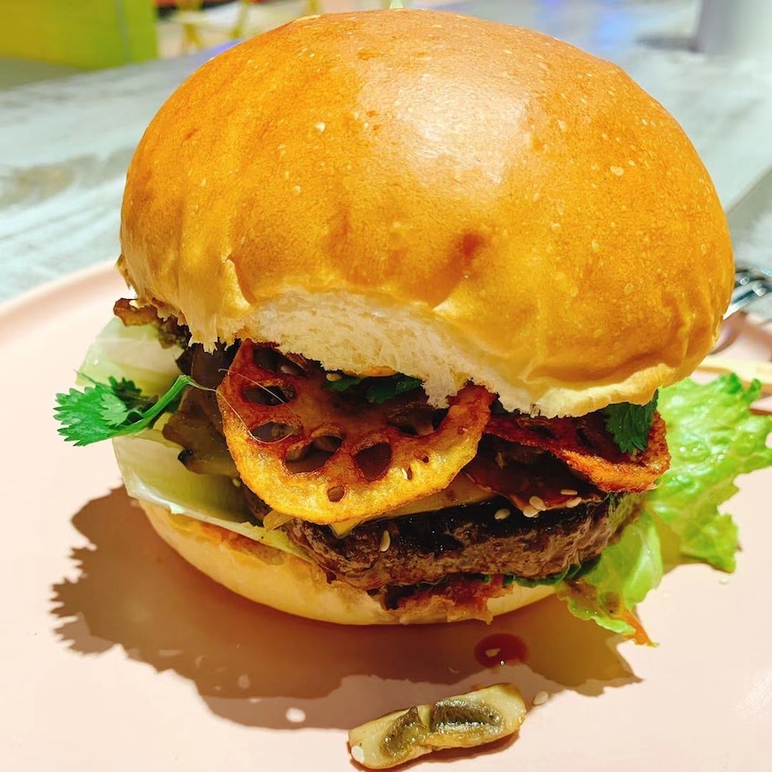 An Aussie burger mixed with fried vegetables and hot pot sauce placed on a table.