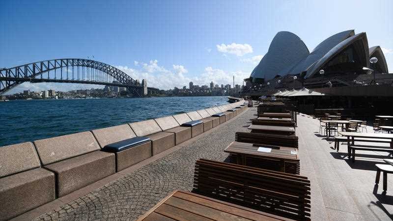Empty tables at a bar in front of the Opera House.