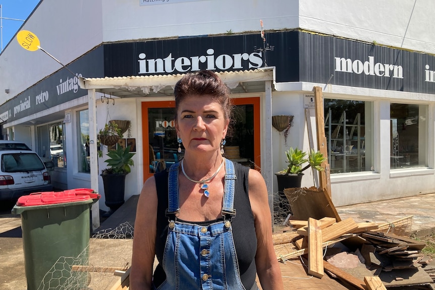 A woman in blue overalls stands outside a homewares shop.
