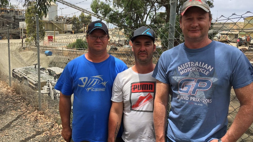 Three men stand outside a fenced area