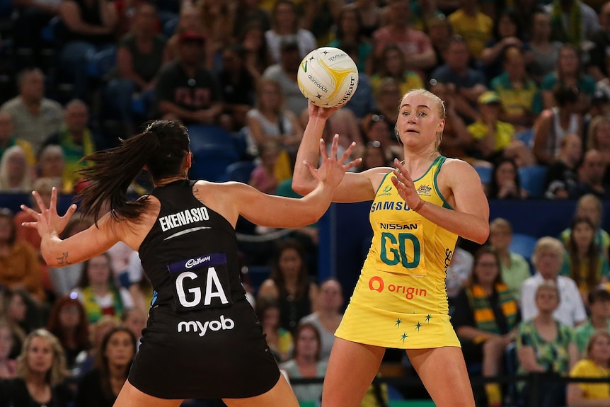 Netballer in the action of throwing the ball with defender with her arms up during a match