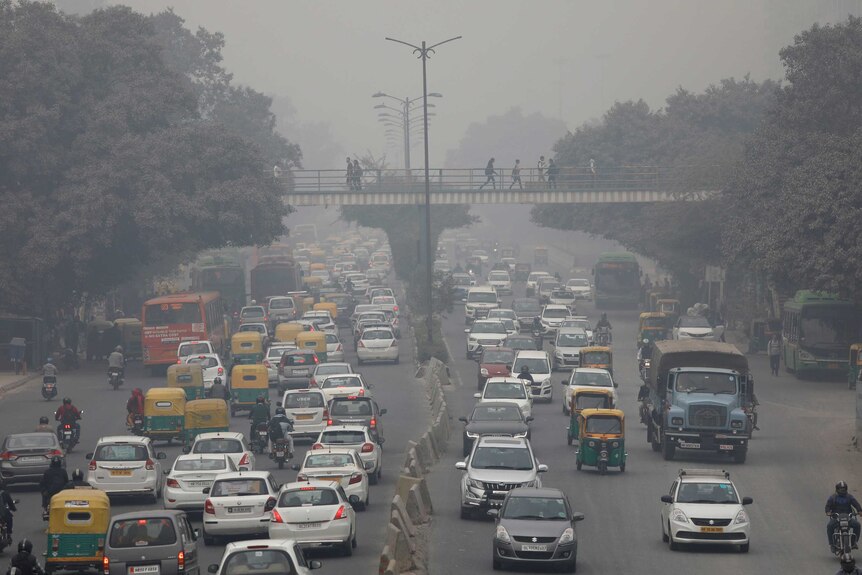 Several lanes of traffic drive through smog that limits visibility.