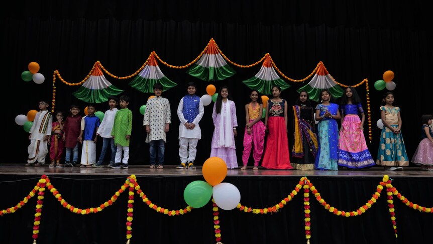 Children dressed in colourful Indian costumes lined up on a stage with orange, green and white decorations