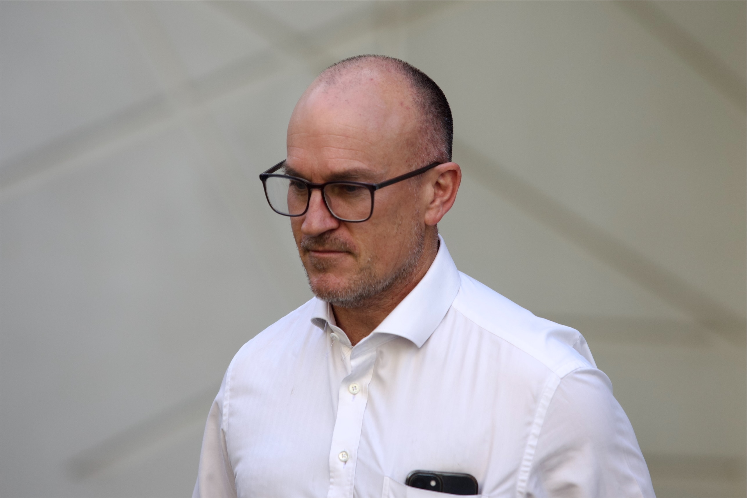 Un hombre con gafas y camisa de negocios camina frente a un gran edificio.