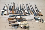 25 firearms laying on a tiled floor