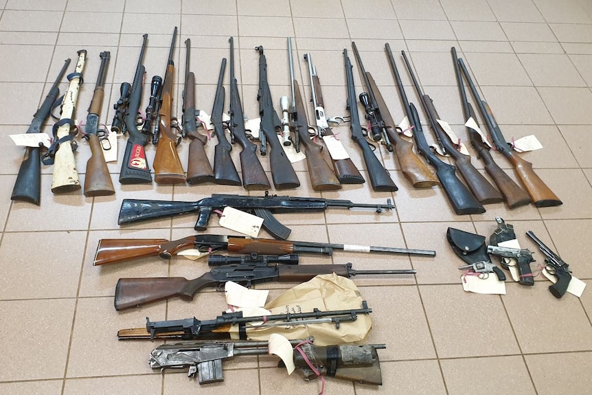 25 firearms laying on a tiled floor