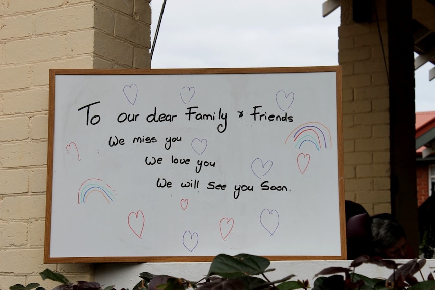 A white sign with writing in texta says 'we miss you' to family and friends of aged care residents.