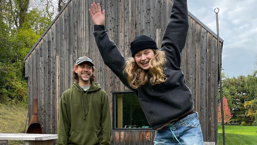 A photo of girl in red jumping in the air next to producer Aaron Dessner outside his Long Pond recording studios