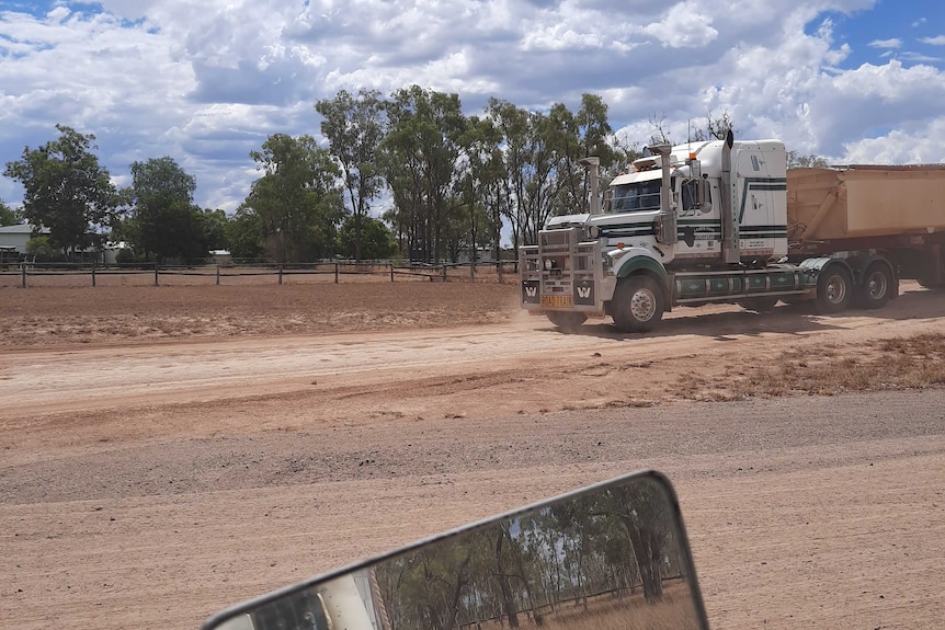 a truck drives past a house on a dirt road