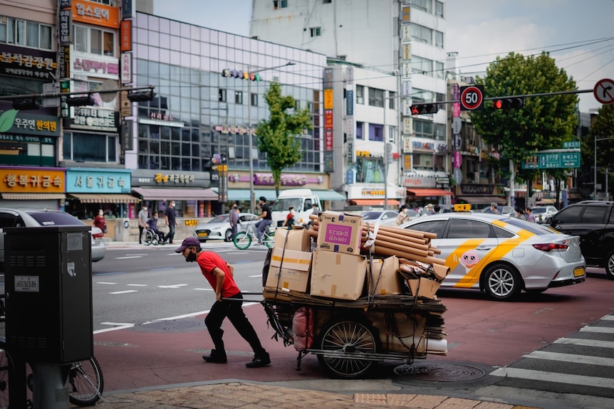 A man pulls a wagon stacked with cardboard through a busy Seoul street
