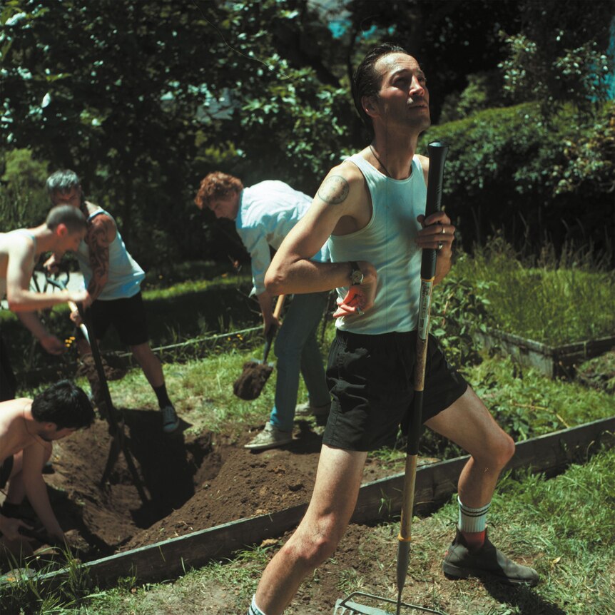 marlon williams and three other men doing manual labour wearing singlets and shorts and holding garden tools