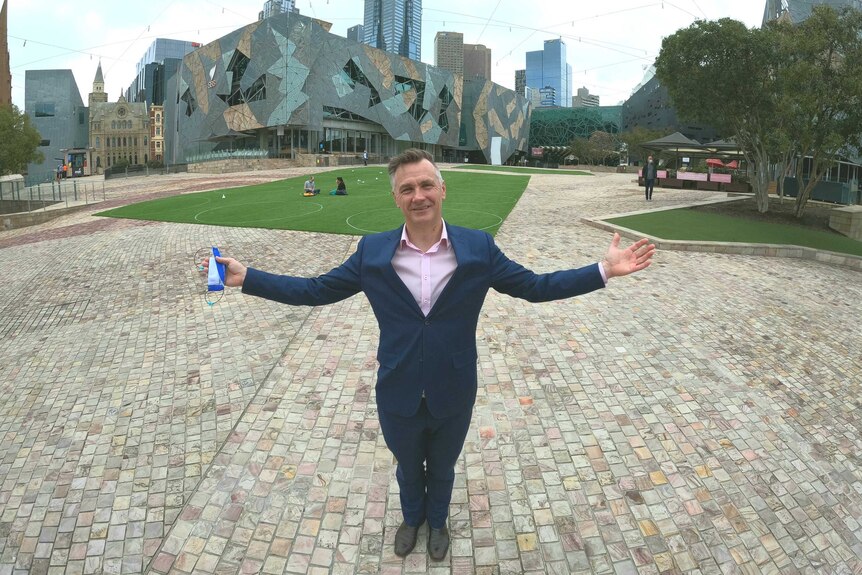 Man holds his hands out with Federation Square in the backdrop.