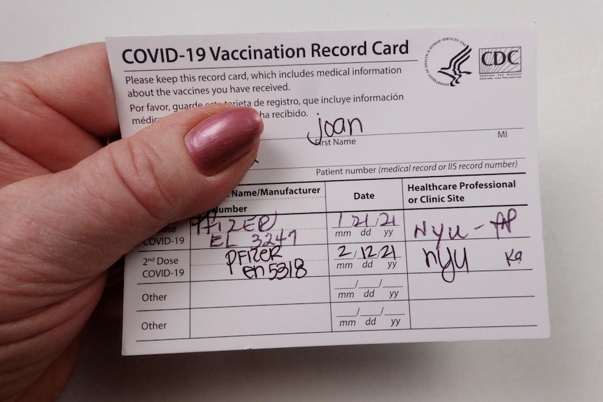 A woman's hand holding a card with vaccine details