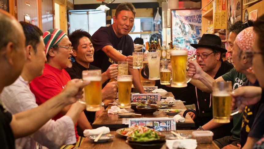 A group of smiling men seated around a table raise their glasses of beer in a toast.