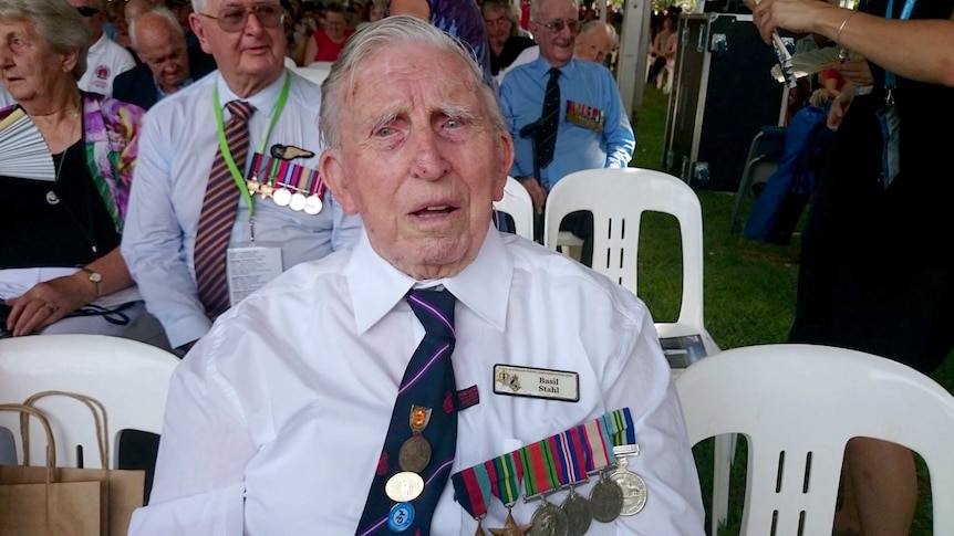 Bombing of Darwin veteran Basil Stahl, 90, is seated at a commemoration service, displaying medals pinned to his white shirt.