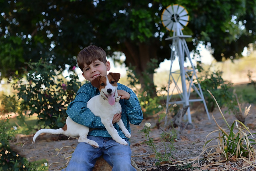 A 7 year old boy plays with his dog in front of a small windmill