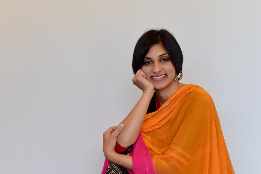 A woman in an Indian sari smiles in front of a white backdrop