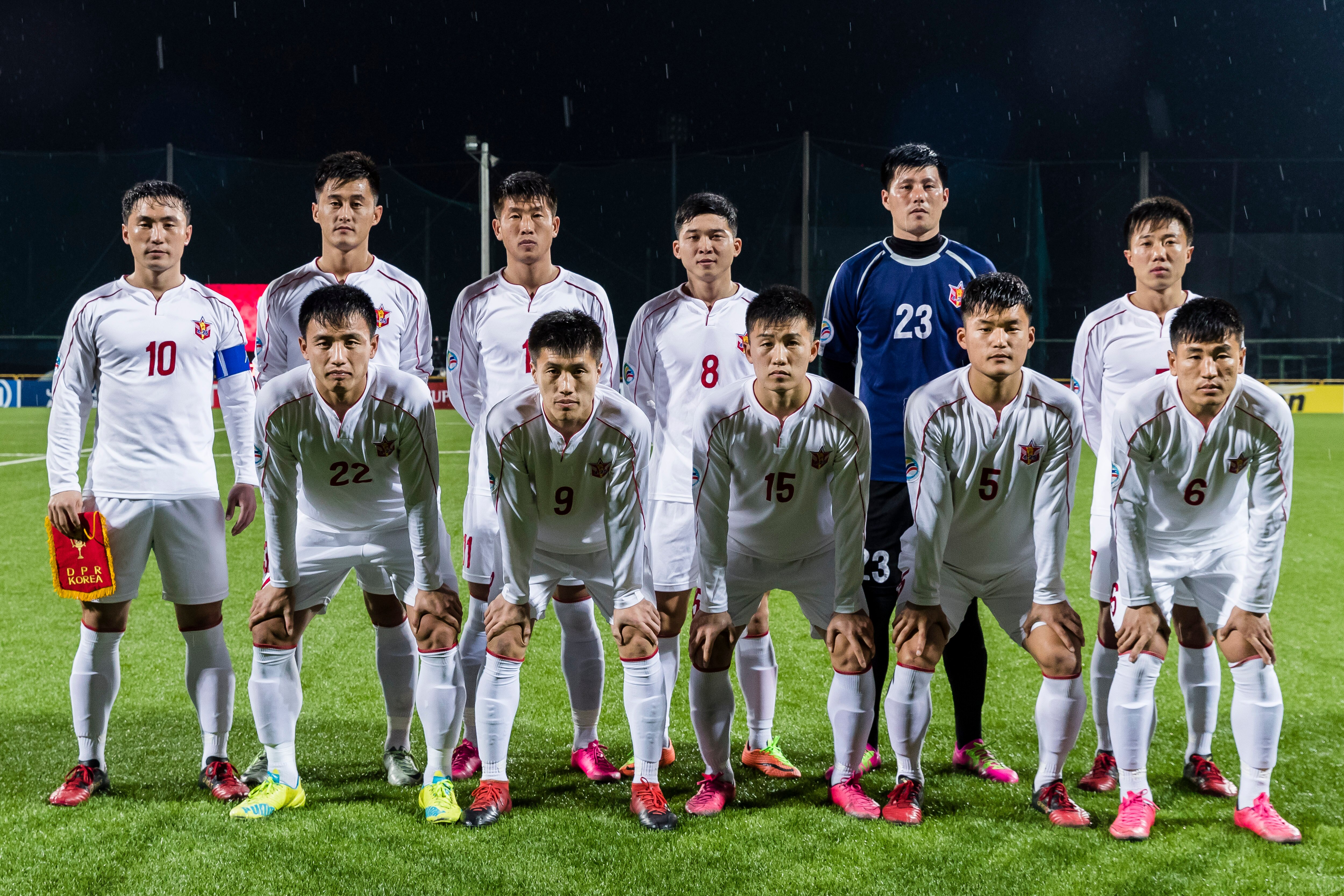 A soccer team wearing white and red poses for a photo before a game while standing in two lines