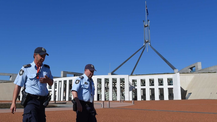Two police officers walk past the front of Canberra Parliament House. The sky is bright blue.
