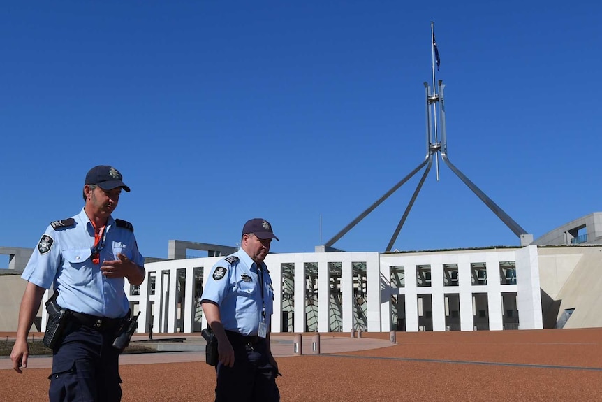 Two police officers walk past the front of Canberra Parliament House. The sky is bright blue.
