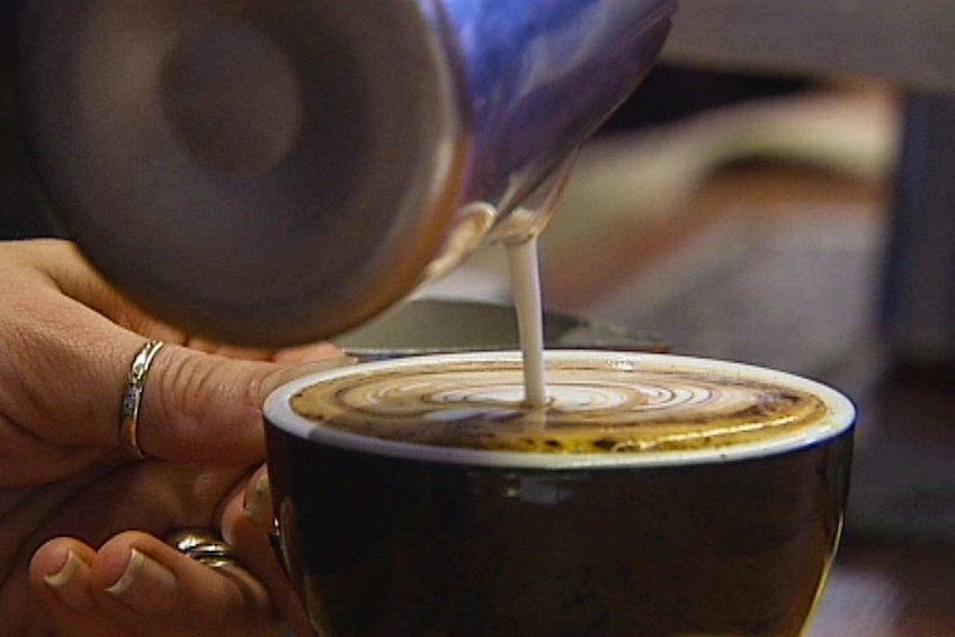 A barista pours hot milk into an espresso coffee