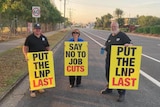 Three people holding signs on the side of a road. Two signs say "put the LNP last", the other sign says "say no to job cuts"