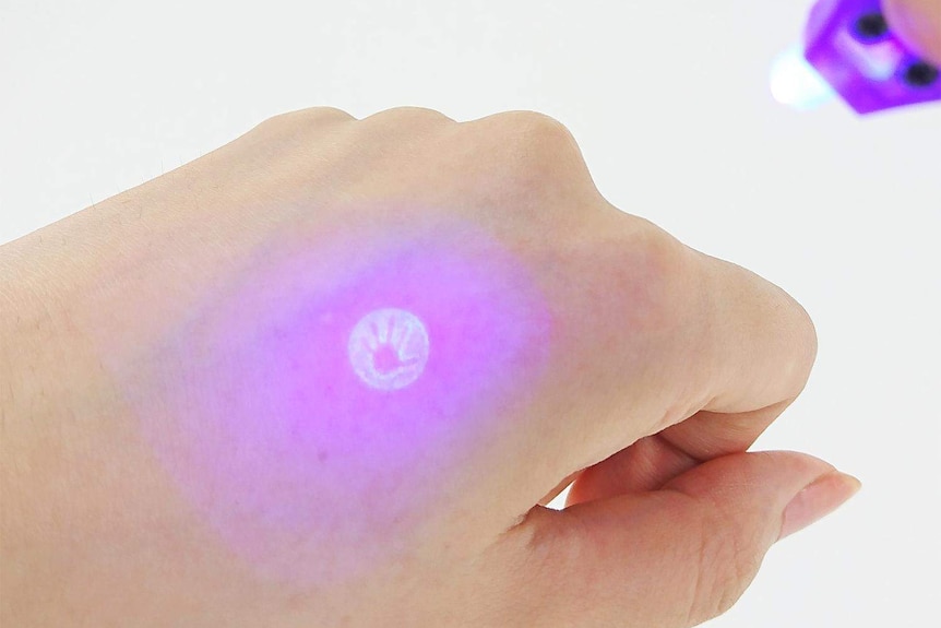 An ultraviolet light shines up a hand-shaped mark on a hand.