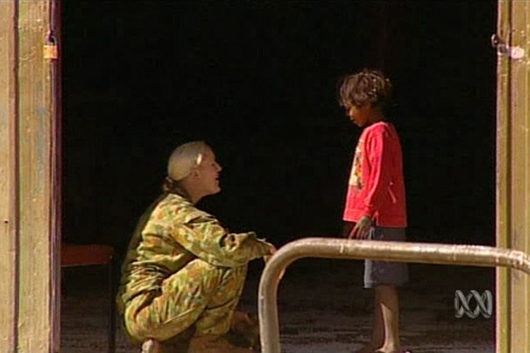 A woman in camo talks to a young child.