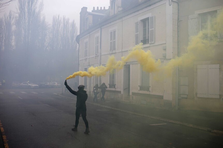 In the city of Bourges, a lone protester walks down a traditional French street with smoke grenade emitting yellow smoke.