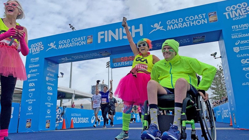 Brett Morris sits in a wheel chair smiling at the marathon finish line.