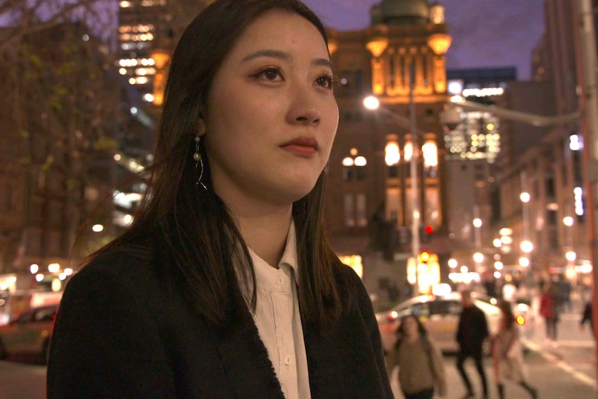 Iris Yao standing on a Sydney street at night time, wearing a black jacket and white shirt