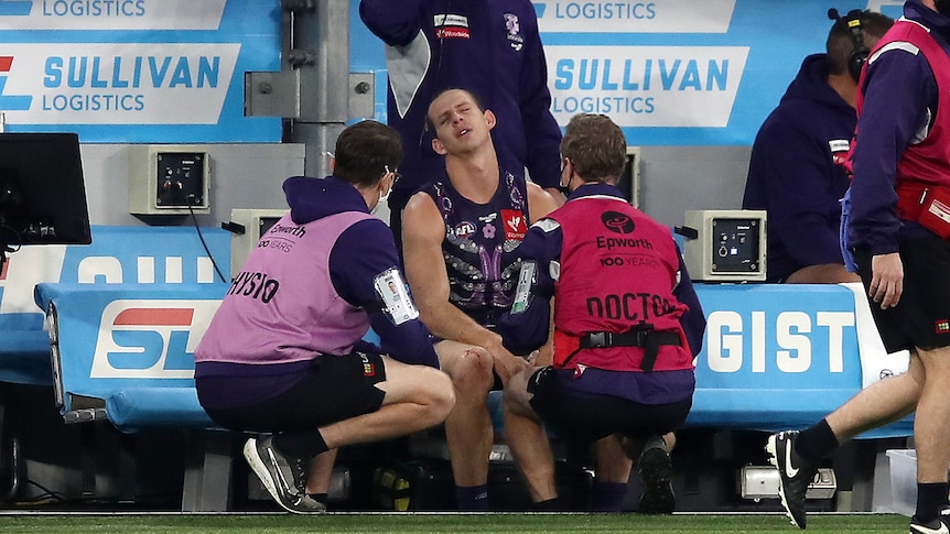 Fremantle AFL star Nat Fyfe grimaces in pain as he is treated for a shoulder injury on the sidelines during a game. 
