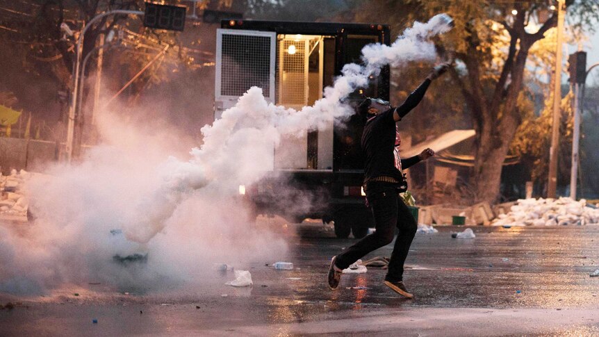 An anti-government protester throws a tear gas canister back at riot police.