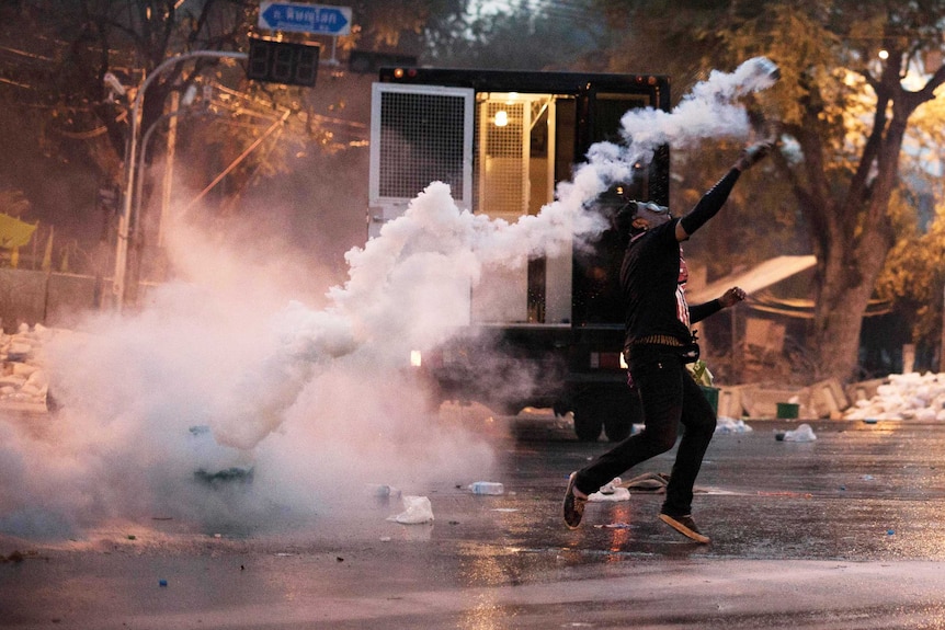 An anti-government protester throws a tear gas canister back at riot police.