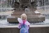 A child in a fairy costumer is on her own staring at a wishing well