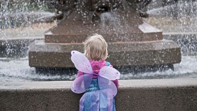 A child in a fairy costumer is on her own staring at a wishing well