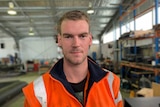 Jake Hartshorn, wearing high-visibility clothing, stands in a factory.