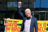 David McBride raises is hand in a triumphant pose as people hold signs of support behind him.