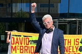 David McBride raises is hand in a triumphant pose as people hold signs of support behind him.