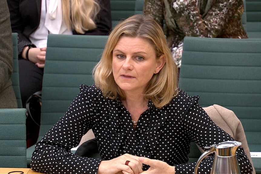 An mature woman with blonde hair is sitting behind a desk in Britain's parliament. She's wearing a black top with white spots.